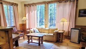 A cozy cabin interior with a wooden floor, a sofa, a table, a lamp, and a refrigerator. - Mazama Trails Laundry House-Dog Friendly&Close to Ski Trail! (Winthrop)