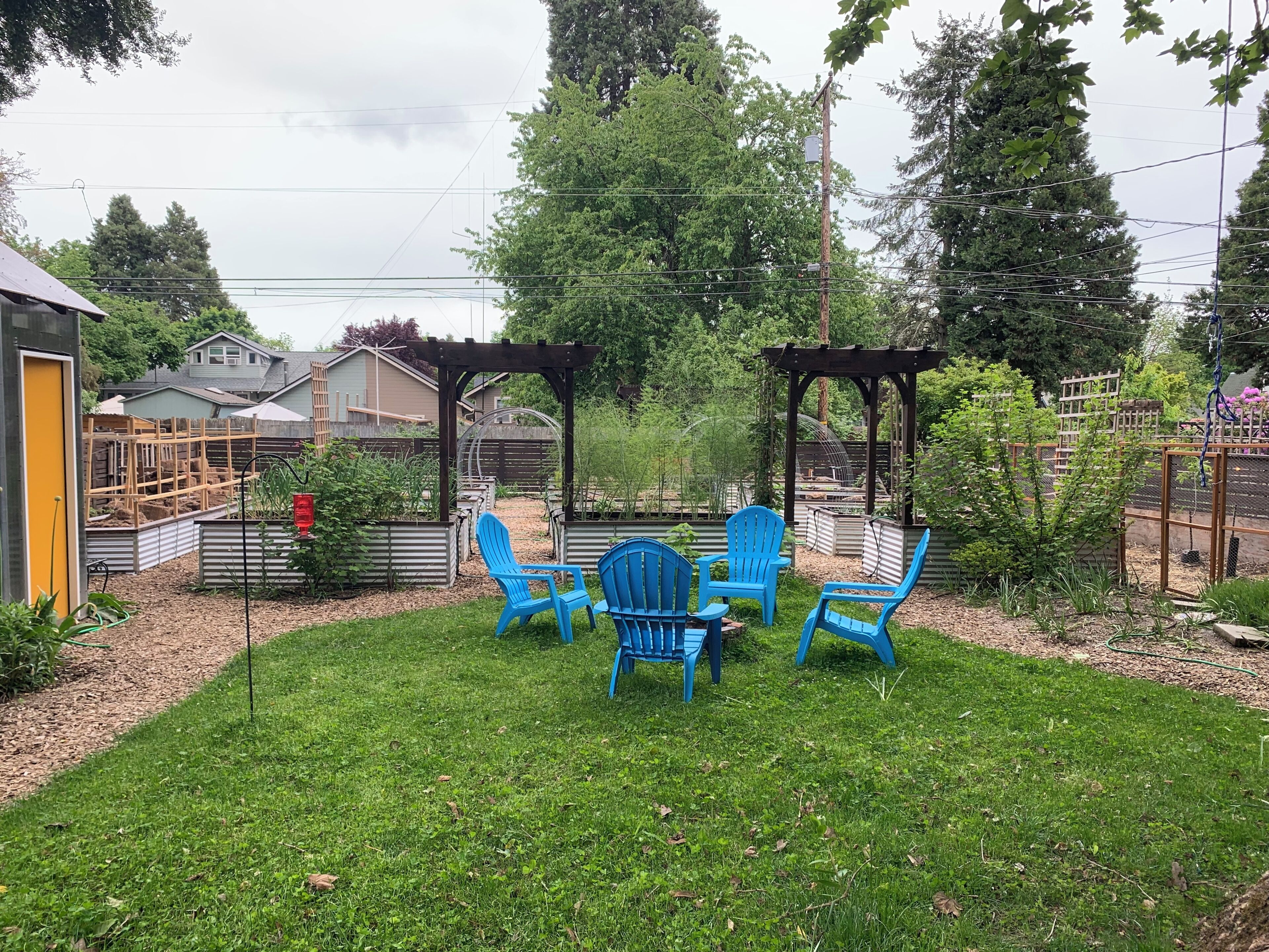 A backyard with a pergola, blue chairs, and raised garden beds.