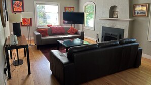 Una sala de estar con sofá, reposapiés, televisor de pantalla plana, chimenea y obras de arte en las paredes.