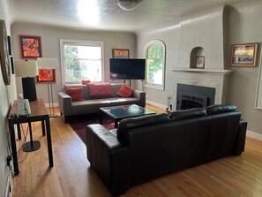 Ein Wohnzimmer mit Sofa, Hocker, Flachbildfernseher, Kamin und Kunstwerken an den Wänden.