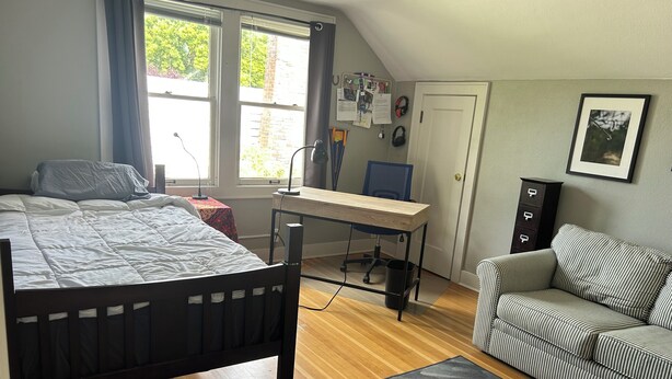 Un dormitorio con cama, escritorio, silla, sofá y ventana con cortinas.