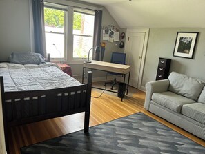 A bedroom with a bed, a desk, a chair, a sofa, and a window with curtains. - Cozy home in Vibrant Whiteaker Neighborhood (Eugene)