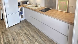 Une cuisine moderne avec des meubles blancs, un plan de travail en bois, un four encastré et un four à micro-ondes.