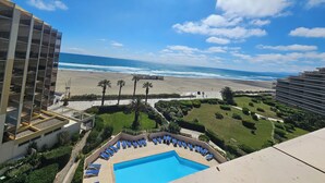Un hôtel doté d’une piscine, offrant une vue sur la plage et bordé de palmiers.