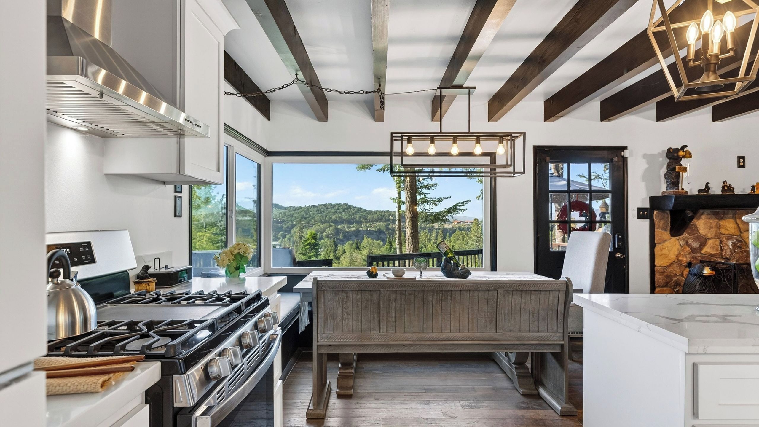 A modern kitchen with a large window, a built-in bench, and a stone fireplace.