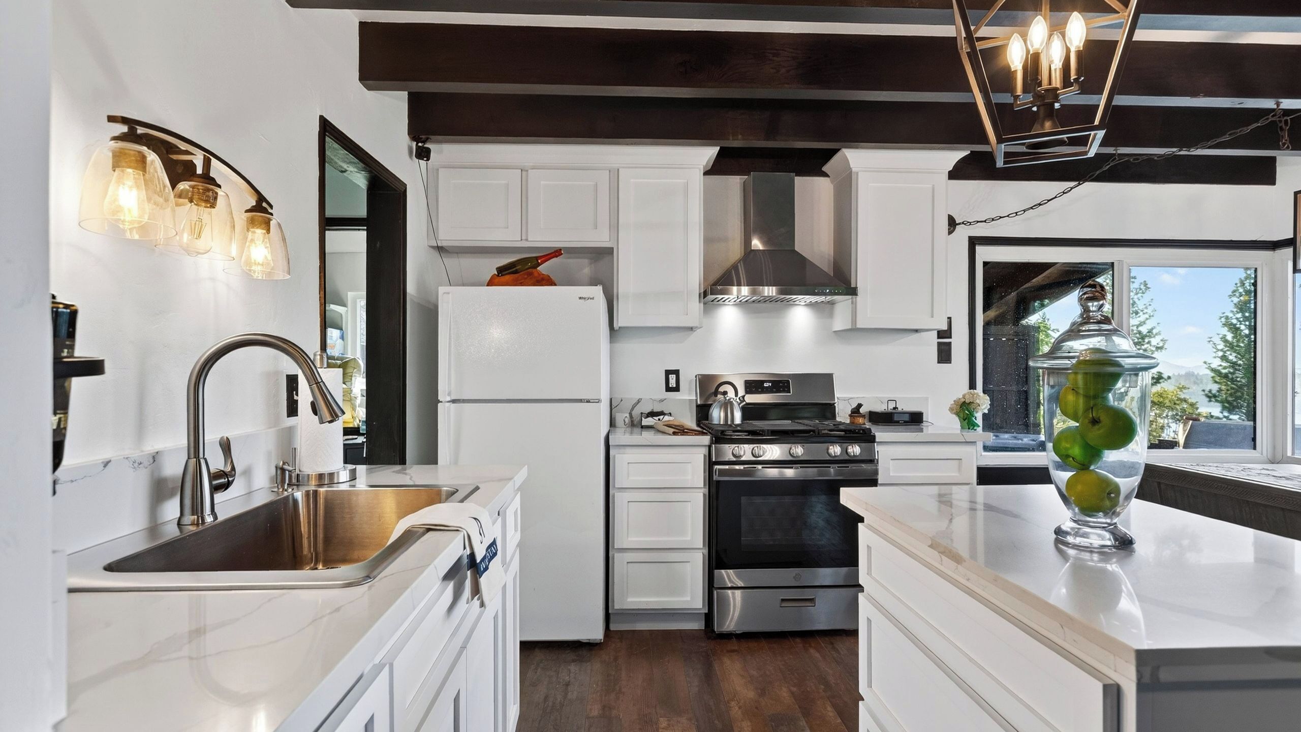 A modern kitchen with white cabinetry, stainless steel appliances, a built-in oven, and a large window offering a view.