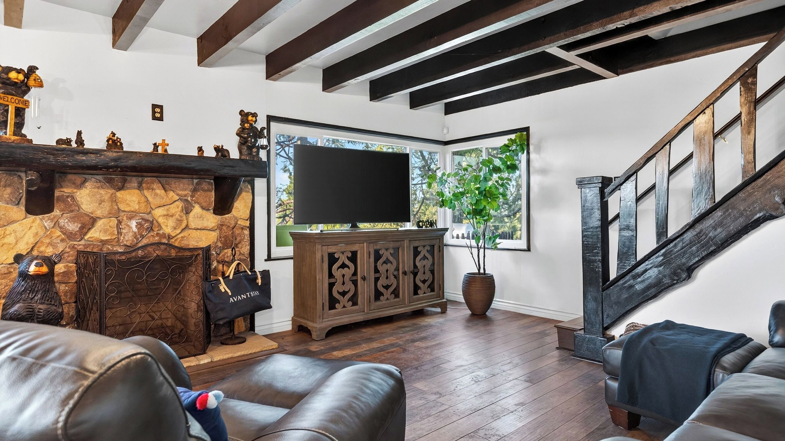 A living room with a stone fireplace, leather furniture, a large flat-screen TV, and a staircase.
