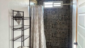 Un baño con inodoro, una estantería metálica, cortina de ducha y azulejos estampados.