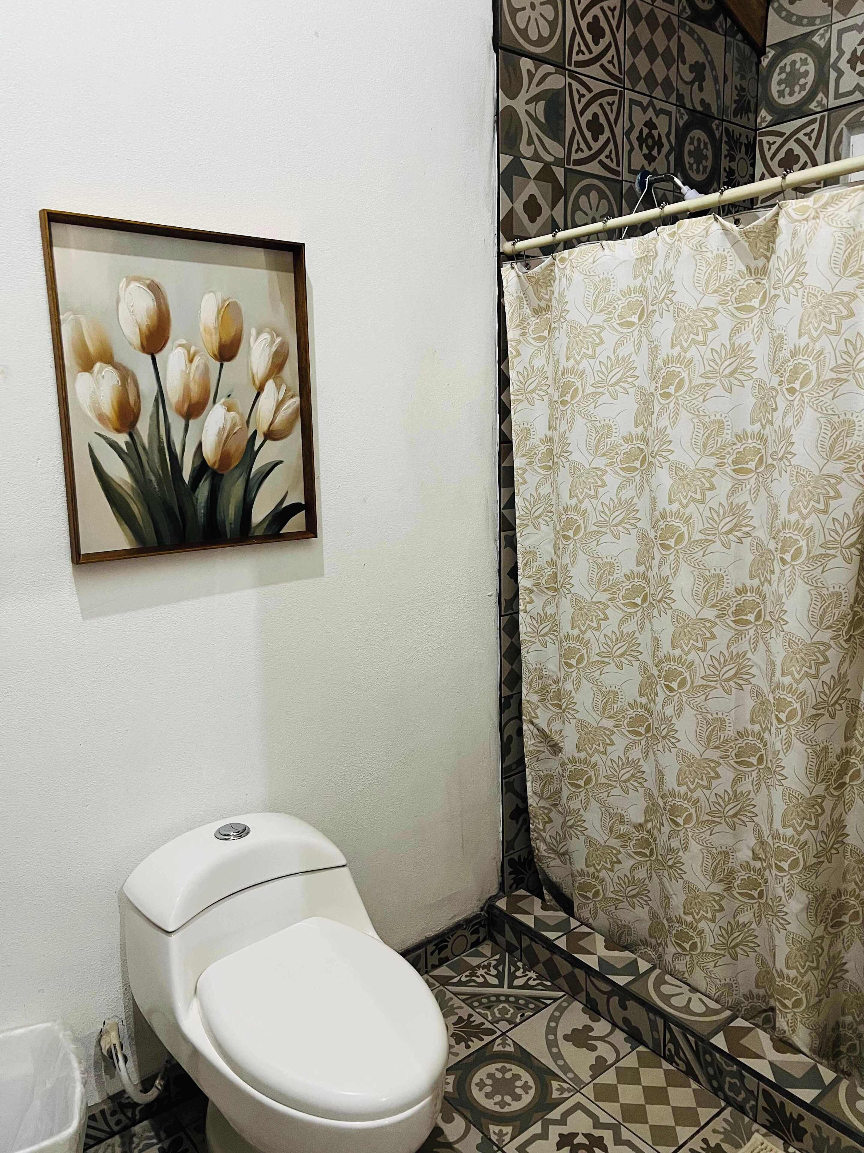 A bathroom with a toilet, a shower curtain with a floral pattern, and a painting of tulips on the wall.