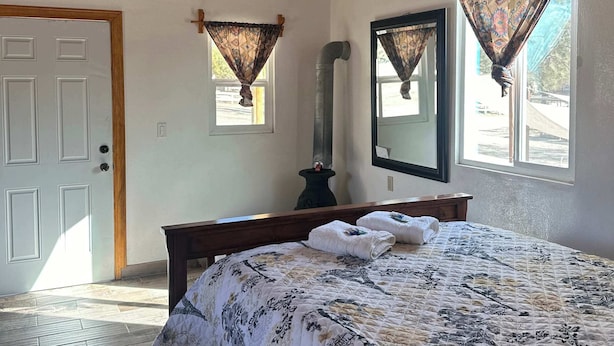 Un dormitorio con techo de madera, una cama con colcha floral, un banco de madera, un espejo y una ventana con cortina.