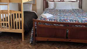 Una habitación con una cama litera de madera, una cama individual con colcha estampada, una ventana con cortinas decoradas y un suelo de madera con patrón de espiga.