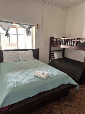 A room with a bed, a bunk bed, a window with curtains, and a wooden floor.