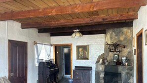 Un interior rústico con techo de madera, chimenea de piedra, un sofá y un tablero de ajedrez.