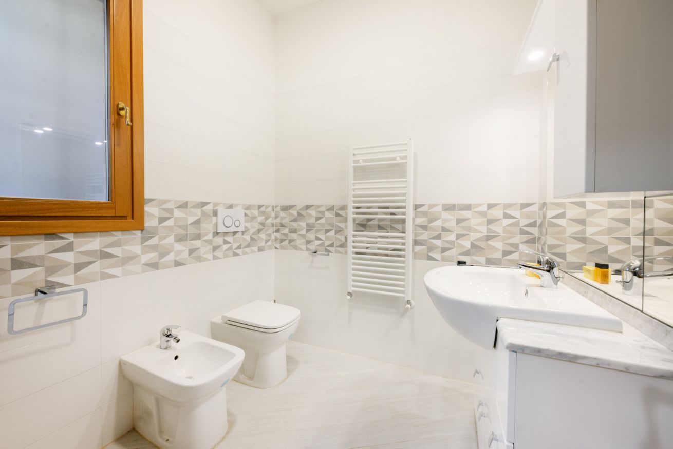 Uma casa de banho moderna com sanita, bidé, lavatório e porta-toalhas.