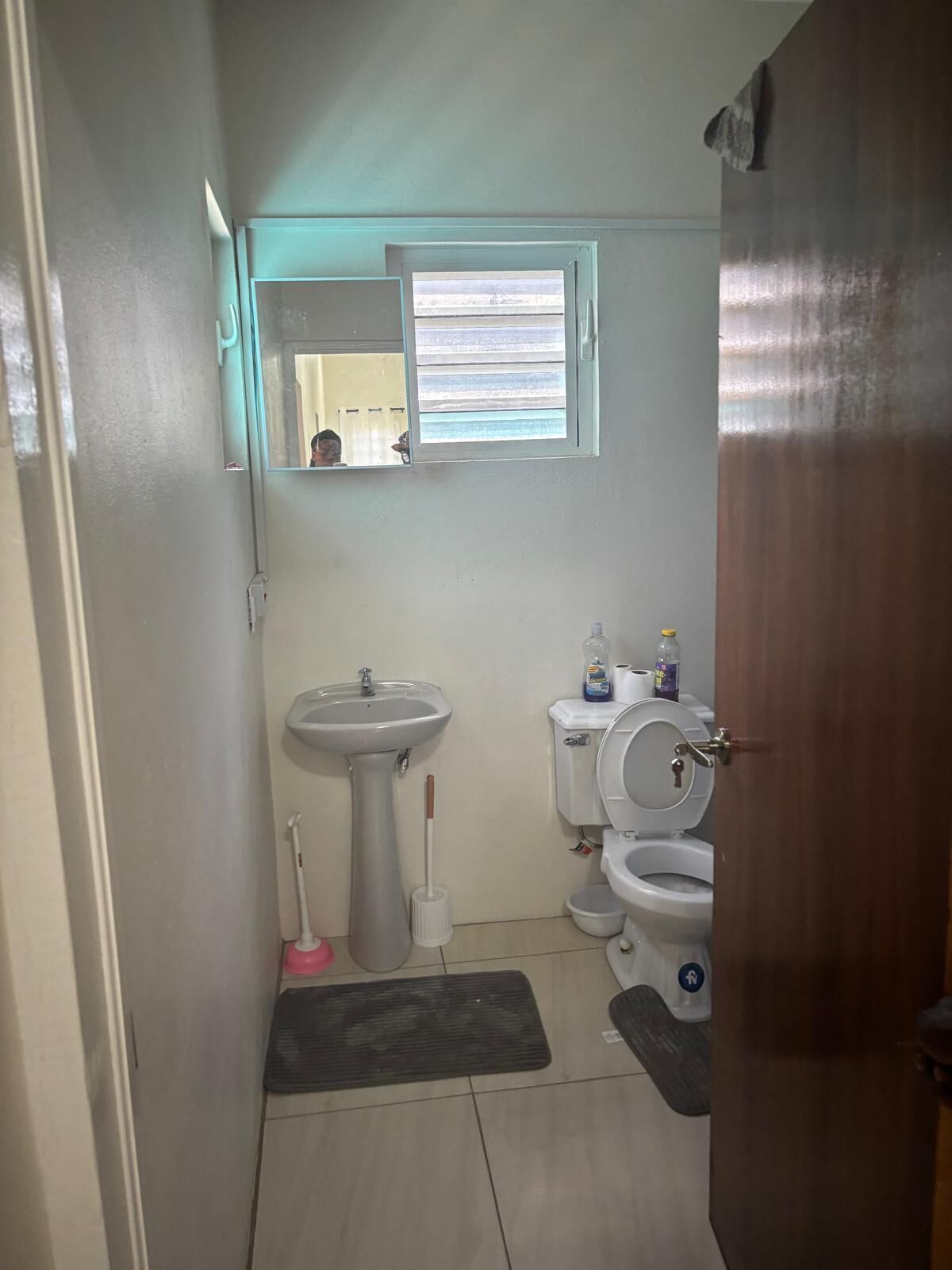 A compact bathroom with a sink, toilet, and bidet. A mirror hangs above the sink, and a window provides natural light.