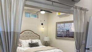 Una camera da letto con un letto, un comodino, una lampada, una sedia, un tavolo in legno e vista sull'esterno.