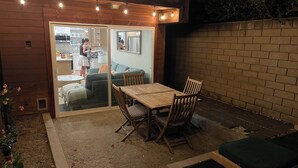 Una terrazza esterna con tavolo e sedie, una porta scorrevole in vetro che conduce a una cucina e un muro in mattoni.