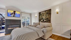 A bedroom with a fireplace, a sofa, a checkered bedspread, and a wall-mounted TV. - Elegant Historic Duplex in Old Town • Lincoln Park (Chicago)