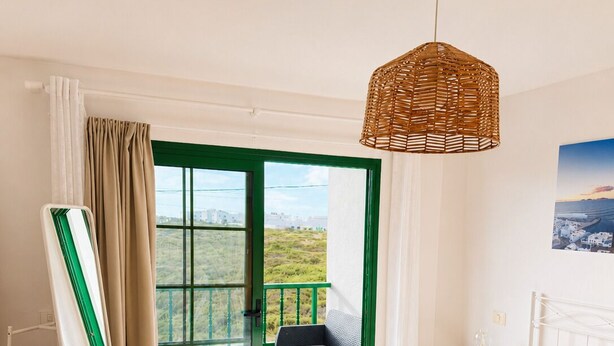 Ein Schlafzimmer mit einem Bett, einem Nachttisch, einer Hängelampe, einem Balkon mit Stuhl und Blick auf die Landschaft.