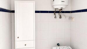 Ein Badezimmer mit weißen Fliesen, einem weißen Heizkörper, einer weißen Waschmaschine und einem weißen Schrank mit Schubladen.