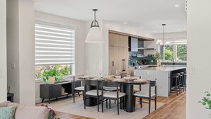 A modern kitchen with a central island, black chairs, and a dining table set for six. - The Shoreline | Luxury Escape w/ Rooftop & Hot Tub (Sylvan Lake)