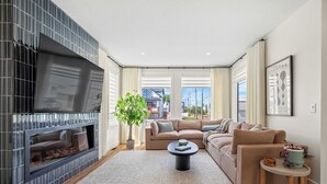 A living room with a fireplace, a large window, a sofa, and a coffee table. - The Shoreline | Luxury Escape w/ Rooftop & Hot Tub (Sylvan Lake)