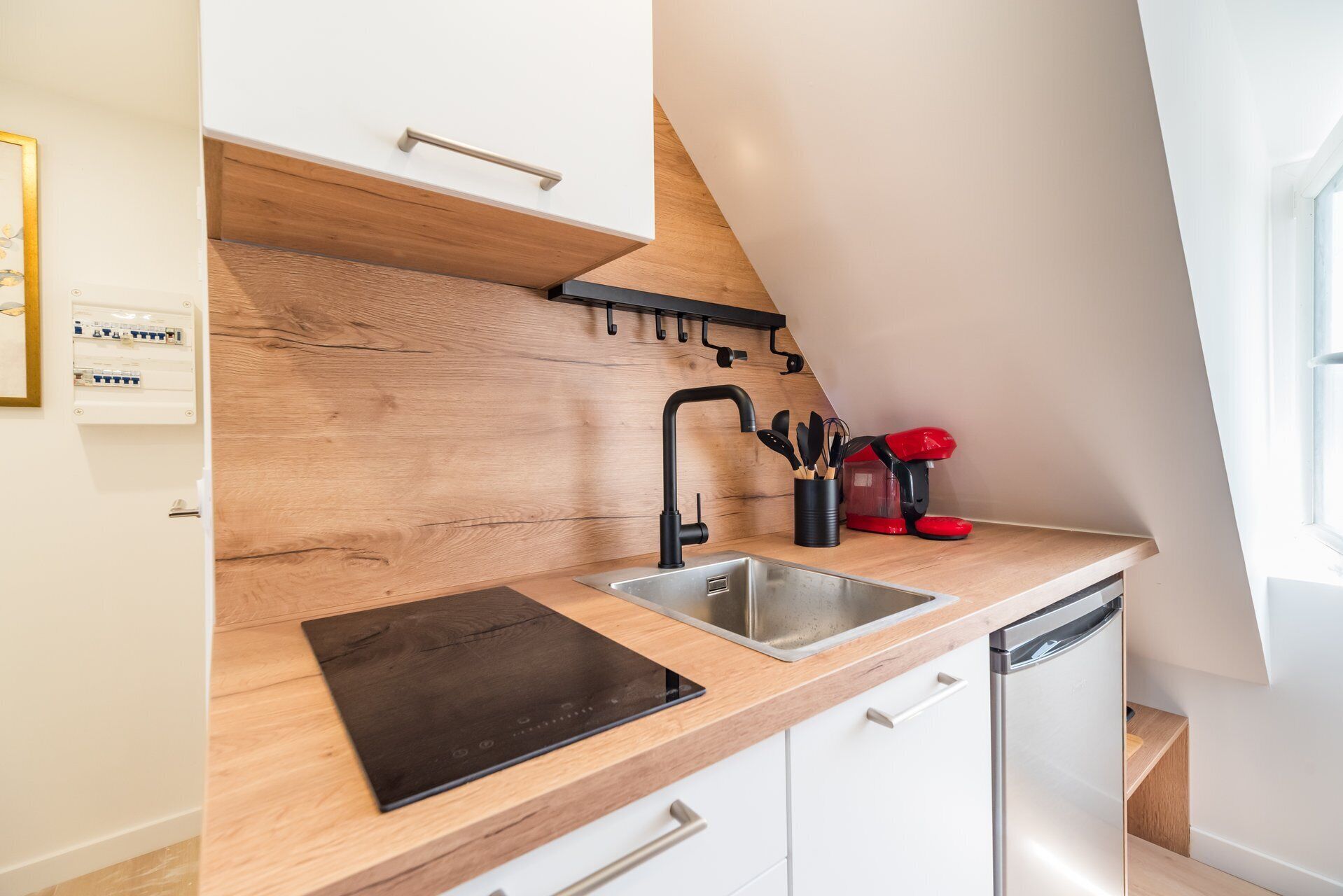 Eine kleine Küche mit einer Holzausziehtheke, einem schwarzen Wasserhahn und einer roten Kaffeemaschine.