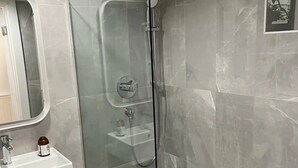 A modern bathroom with a glass-enclosed shower, a white sink, and a marble-tiled floor.