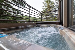 Ein Whirlpool mit Metallgeländer, umgeben von Grünpflanzen und Blick auf einen Hügel.
