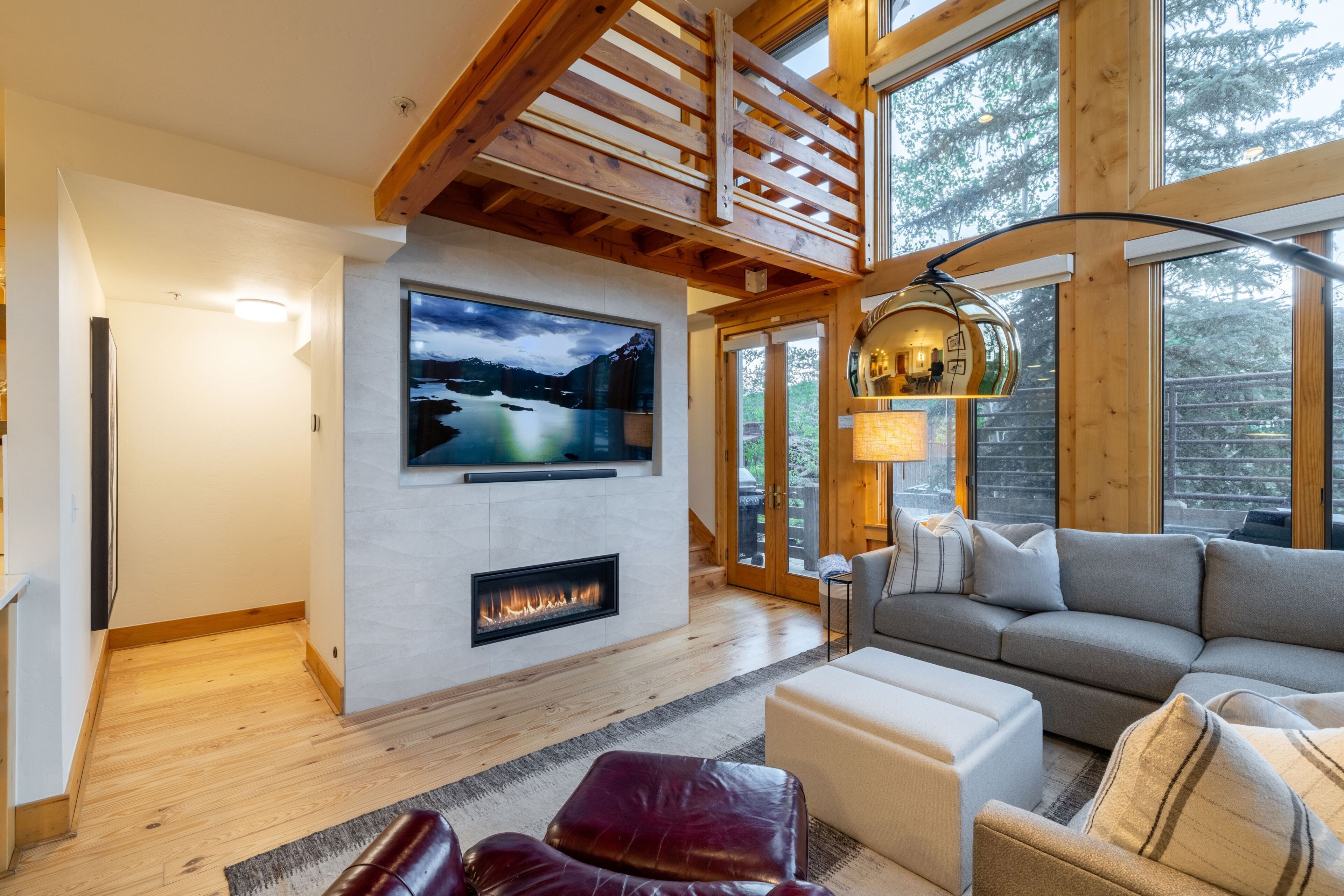 A modern living room with a fireplace, a large TV mounted on the wall, and a cozy seating area with a sofa and ottoman.