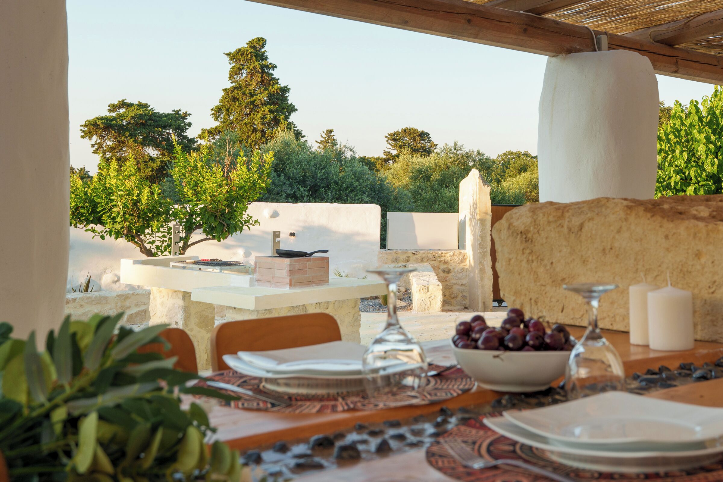 An outdoor dining area with a table set for two, surrounded by stone walls and greenery.