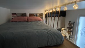 Een slaapkamer met een groot bed, een kledingkast en een plank met diverse spullen.