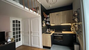 Een kleine keuken met een ingebouwde oven, een spoelbak en een houten aanrecht. Er is een trap die naar een hoger niveau leidt.