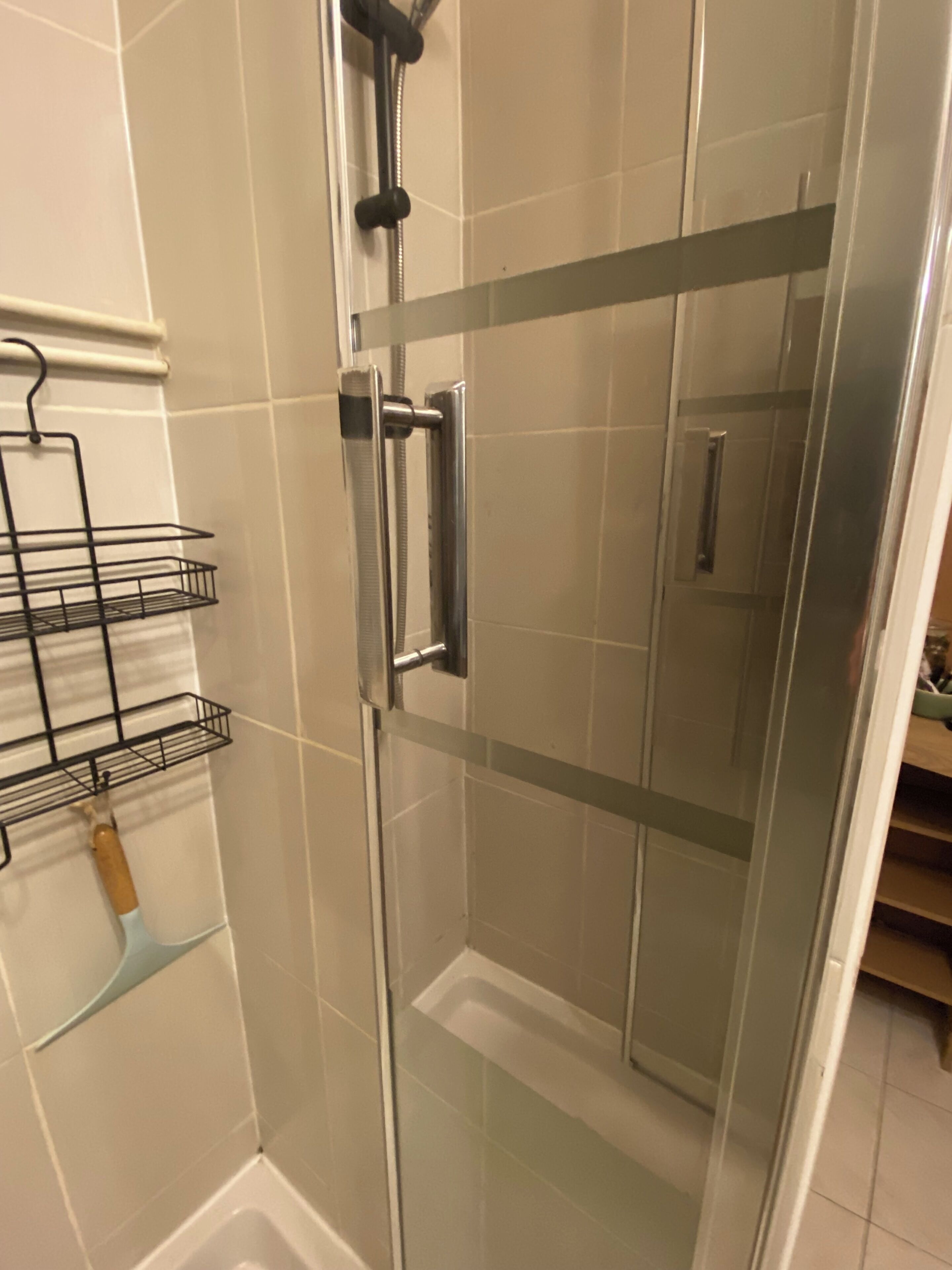 A glass-enclosed shower with a metal handle and a shelf with a brush.
