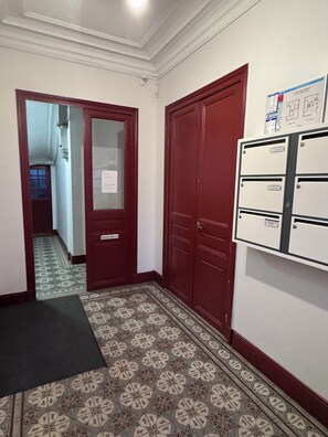 A hallway with patterned floor tiles, a red door, and a utility cabinet with multiple compartments. - Tiny house cozy design at the gates of Paris - Le Pré-Saint-Gervais (Le Pré-Saint-Gervais)