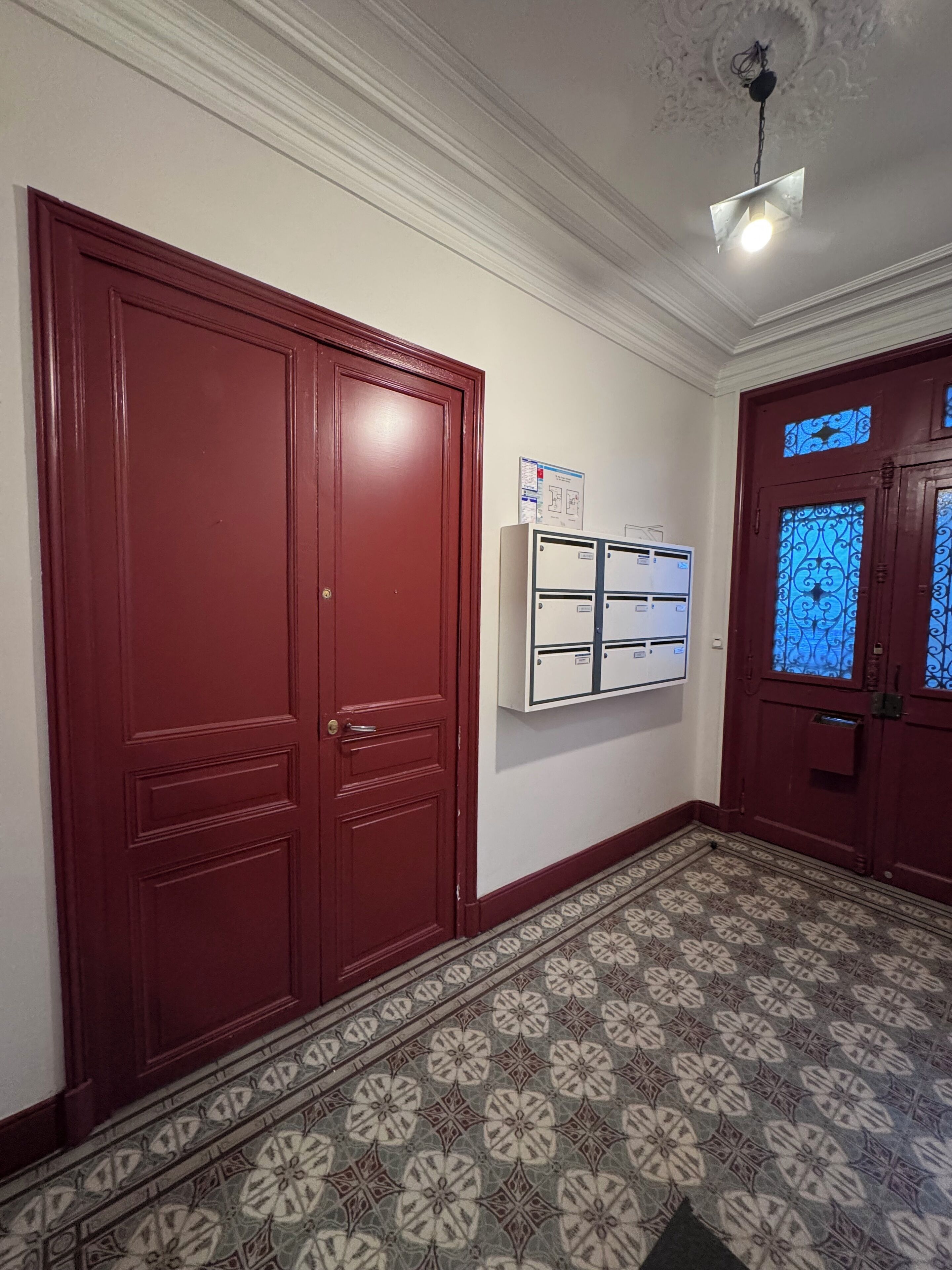 A hallway with patterned flooring, a red door, and a wall-mounted air conditioning unit.