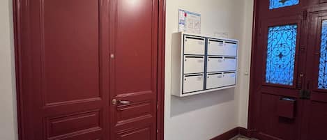 A hallway with patterned flooring, a red door, and a wall-mounted air conditioning unit.