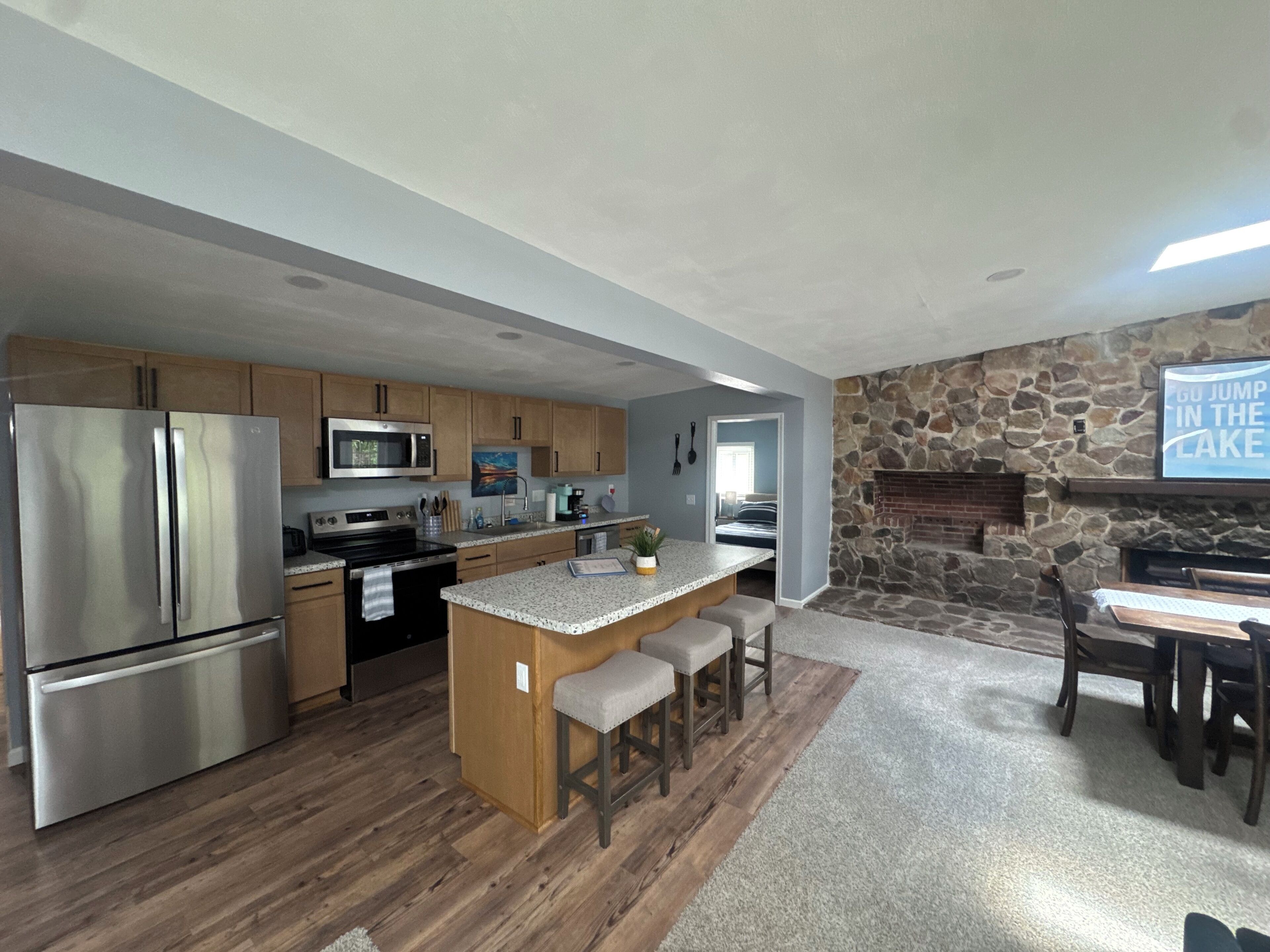 Una cocina moderna con una isla central, armarios de madera, electrodomésticos de acero inoxidable y una chimenea de piedra.
