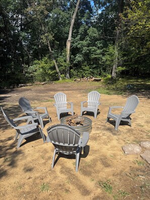 Ein Campingplatz mit vier Adirondack-Stühlen um eine Feuerstelle aus Metall.