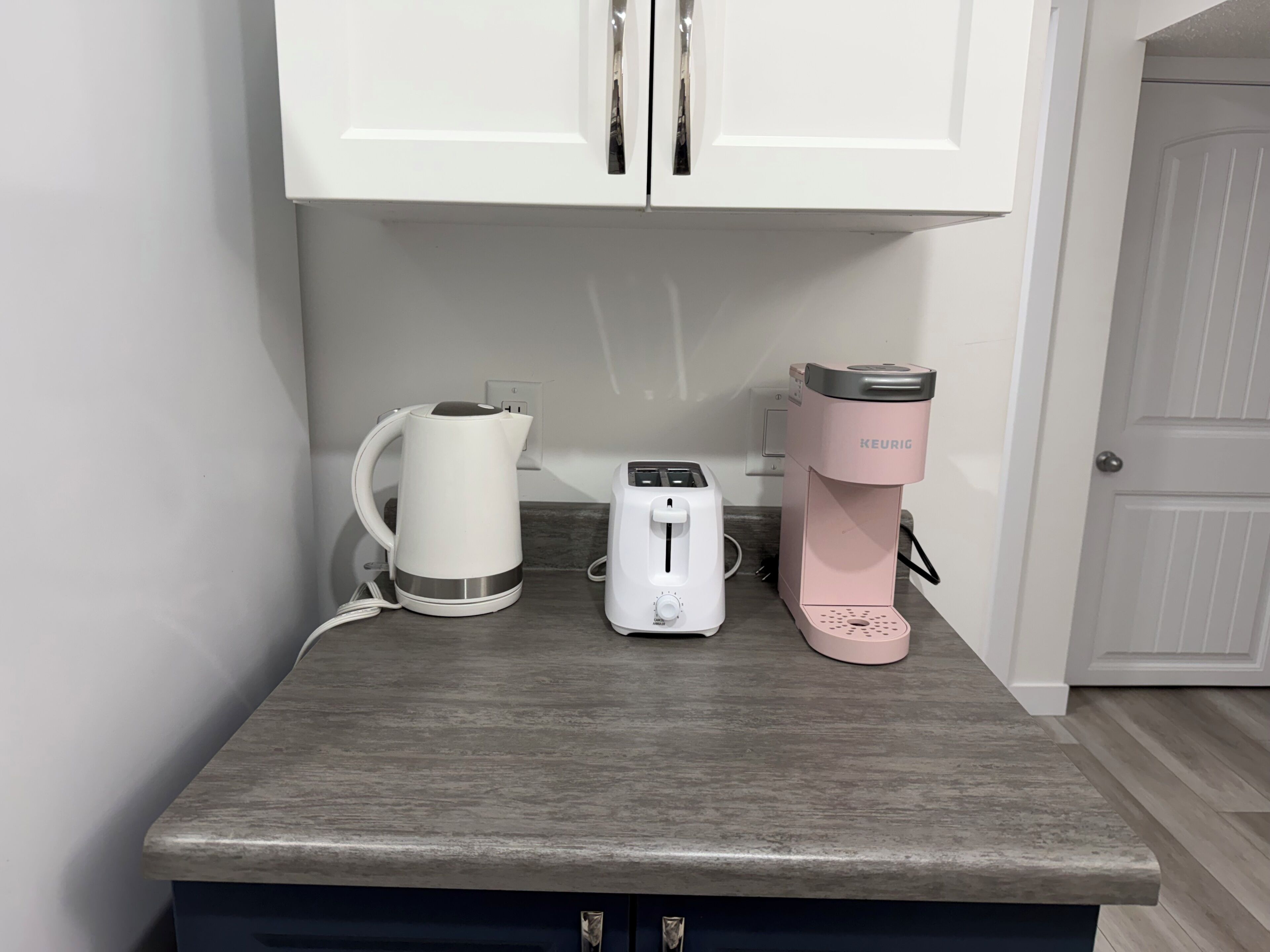 A kitchen counter with a kettle, toaster, and coffee maker.