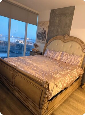 A large bed with a headboard, a nightstand, a framed picture, and a view of a cityscape through large windows. - 2BD/2BR High Rise Condo. In the Heart of Downtown SD (San Diego)