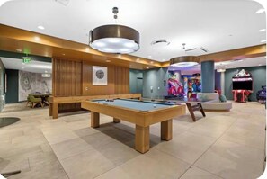 Ein Billardtisch in der Hotelhalle mit einer Neonreklame, einer Bank und einem farbenfrohen Spielautomaten im Hintergrund.
