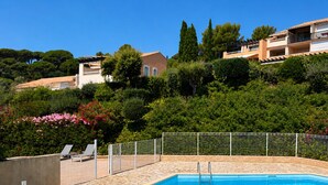 A swimming pool with a tiled deck, surrounded by a metal fence, and houses in the background. - Les Coteaux de la Nartelle, air-conditioned studio with ocean view, pool, sleeps 4 (Sainte-Maxime)