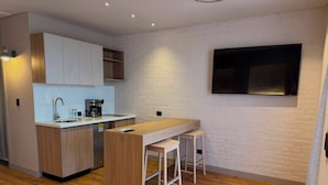A modern kitchen with wooden cabinets, a built-in coffee machine, a sink, and a bar area with stools.