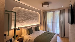 A modern hotel room with a large bed, a bedside table with a lamp, a mirror, and a view of the city through the window.