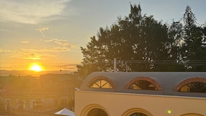 A building with arched windows and a flat roof, surrounded by greenery and a sunset in the background.