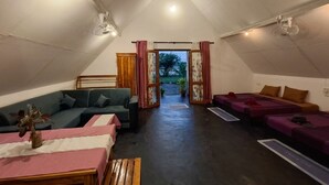 Acogedor dormitorio tipo ático, bien iluminado, con techos altos, amueblado con un sofá, camas y una mesa de comedor.