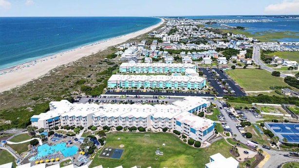 Un complejo turístico frente al mar con varios edificios de hotel, una playa y un estacionamiento.