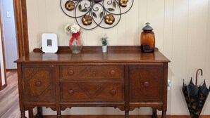 Un comò in legno con cassetti, un elemento decorativo in metallo a parete, un dispositivo bianco sopra, una piccola pianta in vaso e un ombrello.