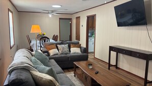 Un soggiorno con un divano, un tavolino in legno, una TV a parete e una zona pranzo sullo sfondo.